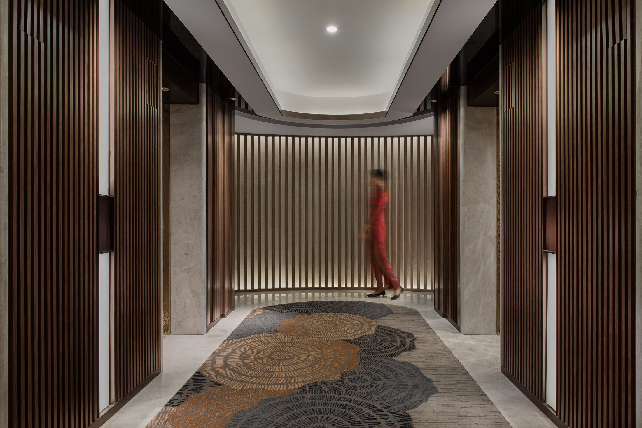 Un pasillo moderno con paneles de madera verticales, alfombra estampada e iluminación empotrada en el techo.