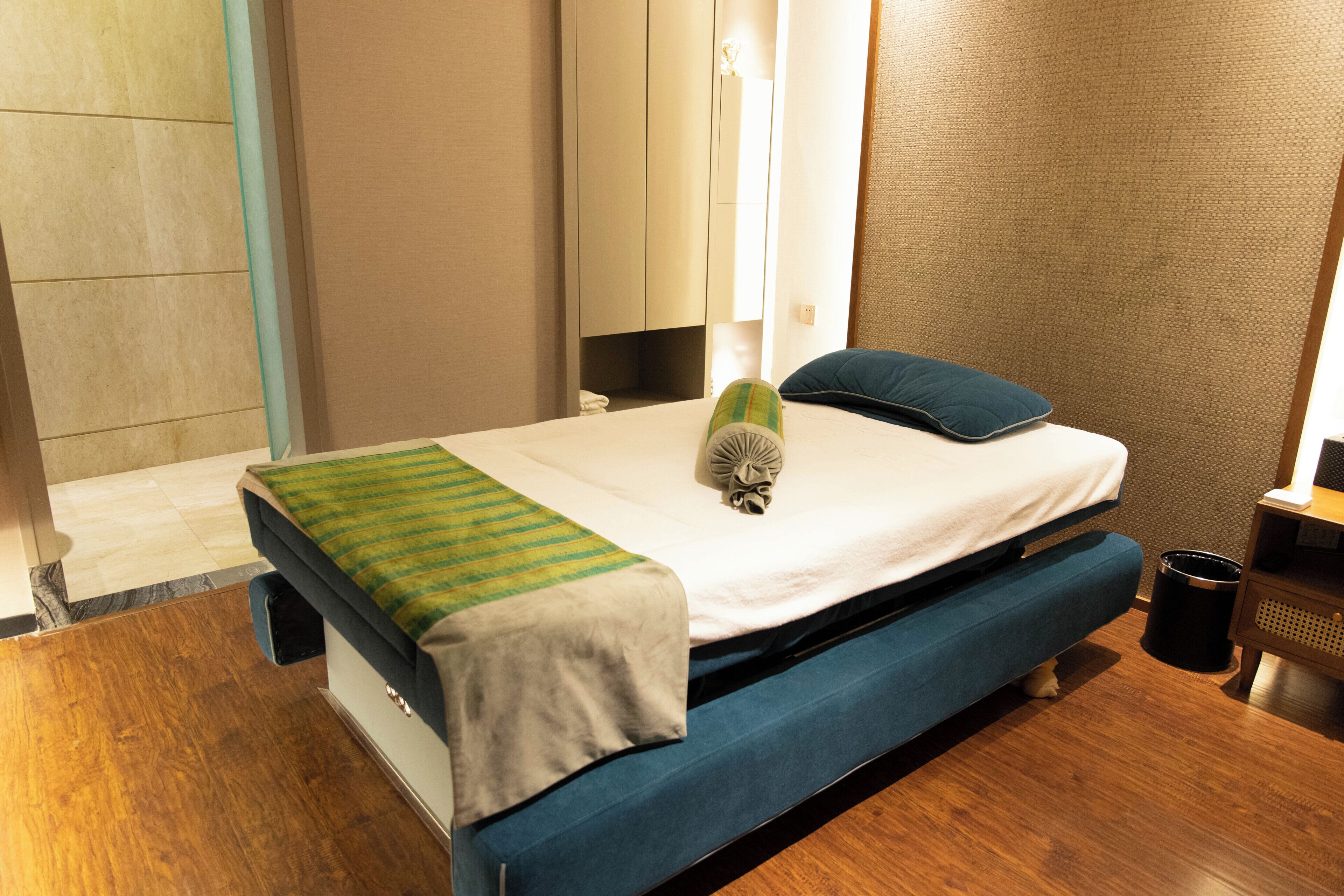 A hotel room with a bed, a bedside table, a trash bin, and a wall with a textured pattern.