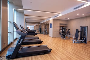 Une salle de sport équipée de tapis de course, d’appareils de musculation et dotée d’un plancher en bois.