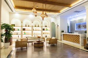 Een hotel lobby met een receptiebalie, een zithoek en decoratieve schapjes.