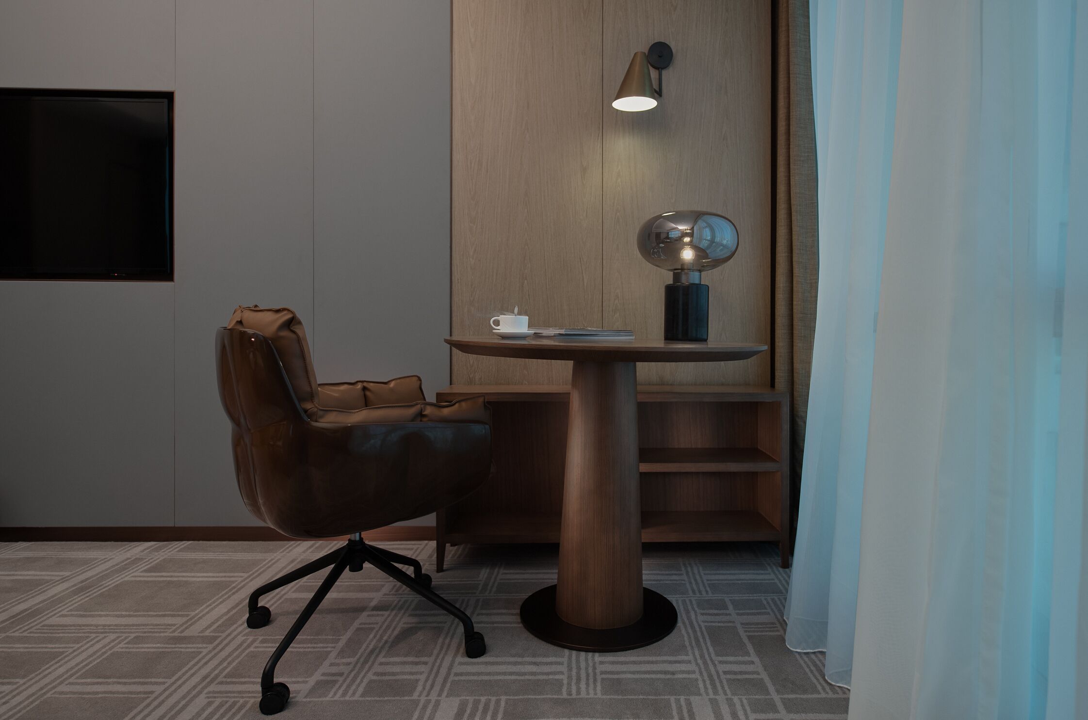 A modern room with a leather chair, a small table with a cup, a wall-mounted lamp, and a mirror.