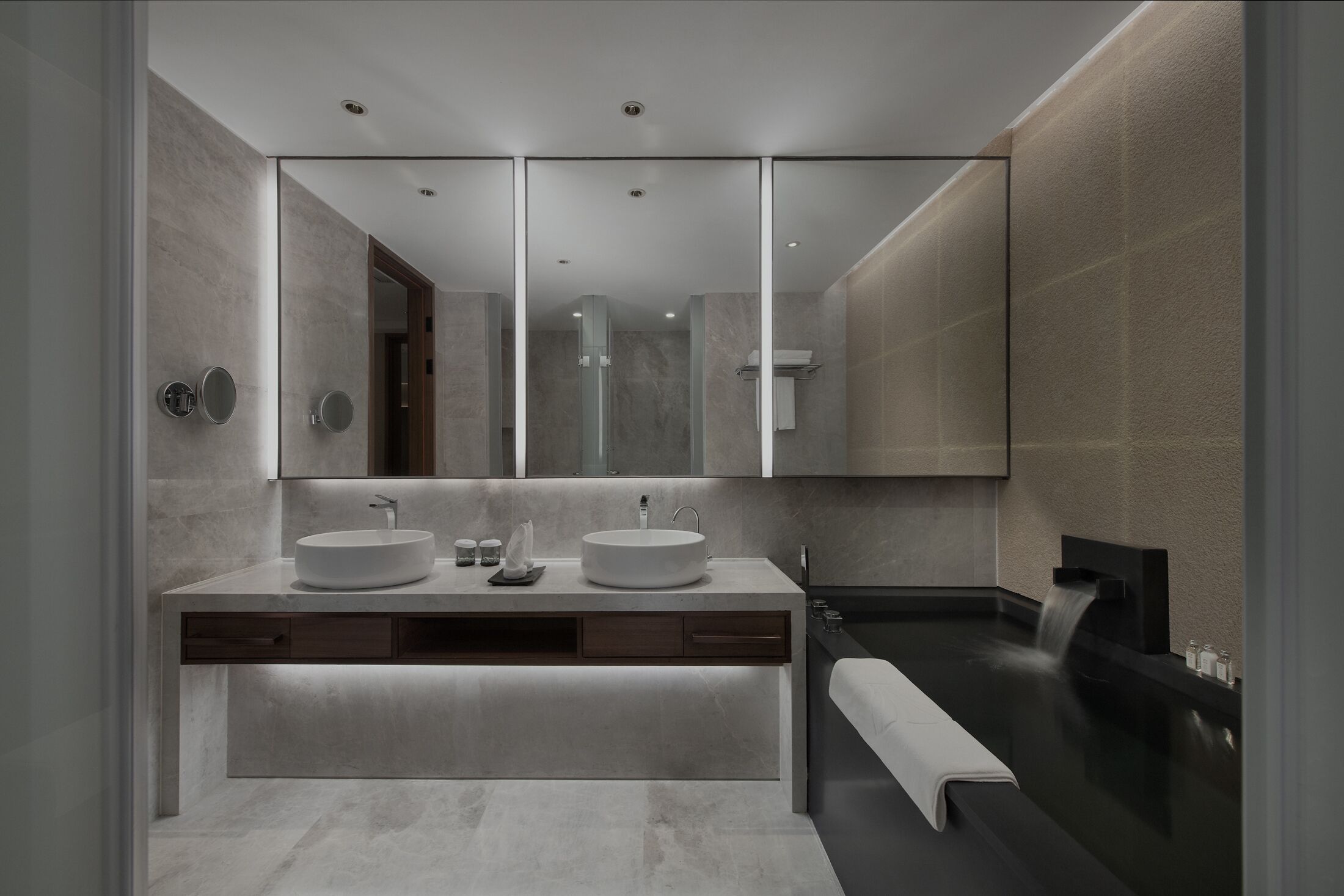 A modern bathroom with a large mirror, two sinks, a bathtub, and a walk-in shower.