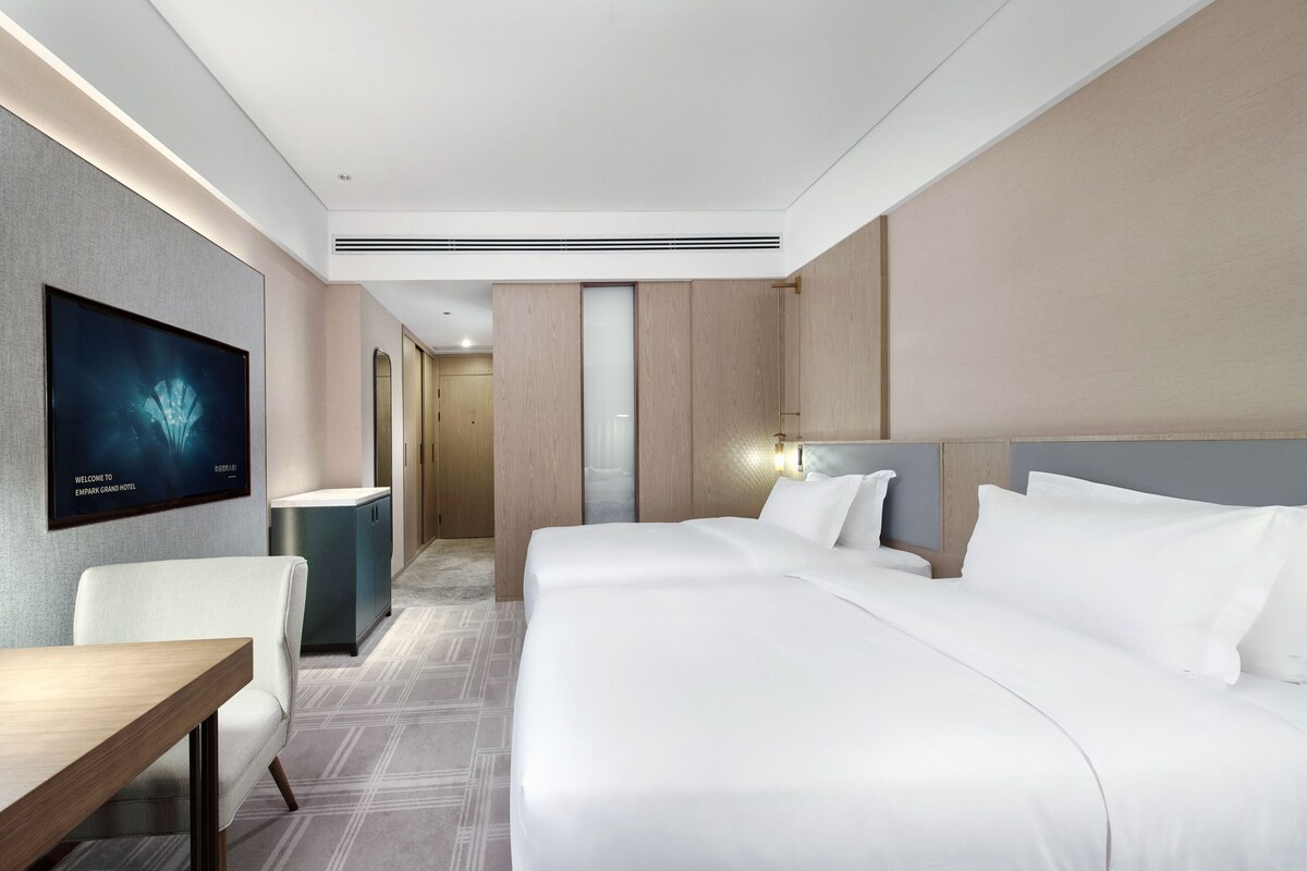 Une chambre d’hôtel comprenant un lit, un bureau, une chaise, un téléviseur fixé au mur et un couloir menant à une autre pièce.