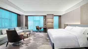 A modern hotel room with a large bed, a sofa, a coffee table, and a desk.