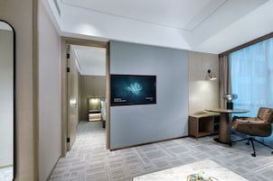 Habitación de hotel con cama, escritorio, silla, televisor y ventana con cortinas.