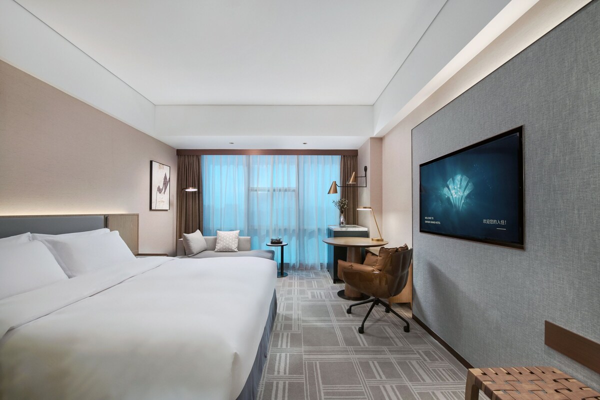 Une chambre d’hôtel avec un grand lit, un bureau, une chaise, une télévision et une vue sur l’extérieur.
