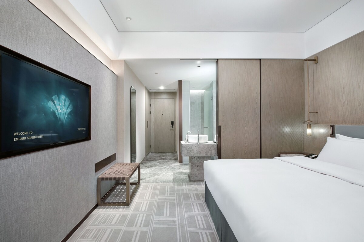 Une chambre d’hôtel moderne dotée d’un grand lit, d’une télévision à écran plat, d’une salle de bain avec un lavabo en marbre et d’un sol à motifs.