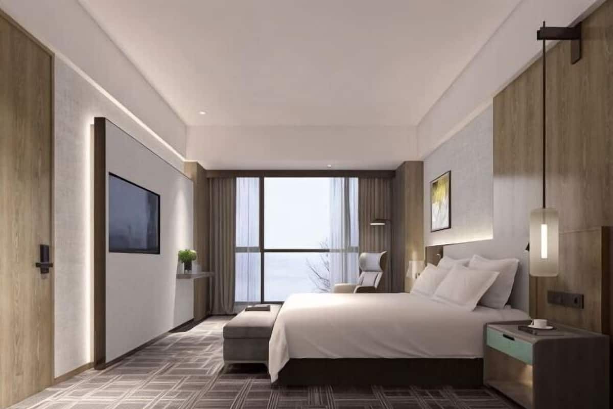 Una habitación de hotel moderna con una cama grande, una mesita de noche y un televisor montado en la pared, además de una ventana con cortinas.