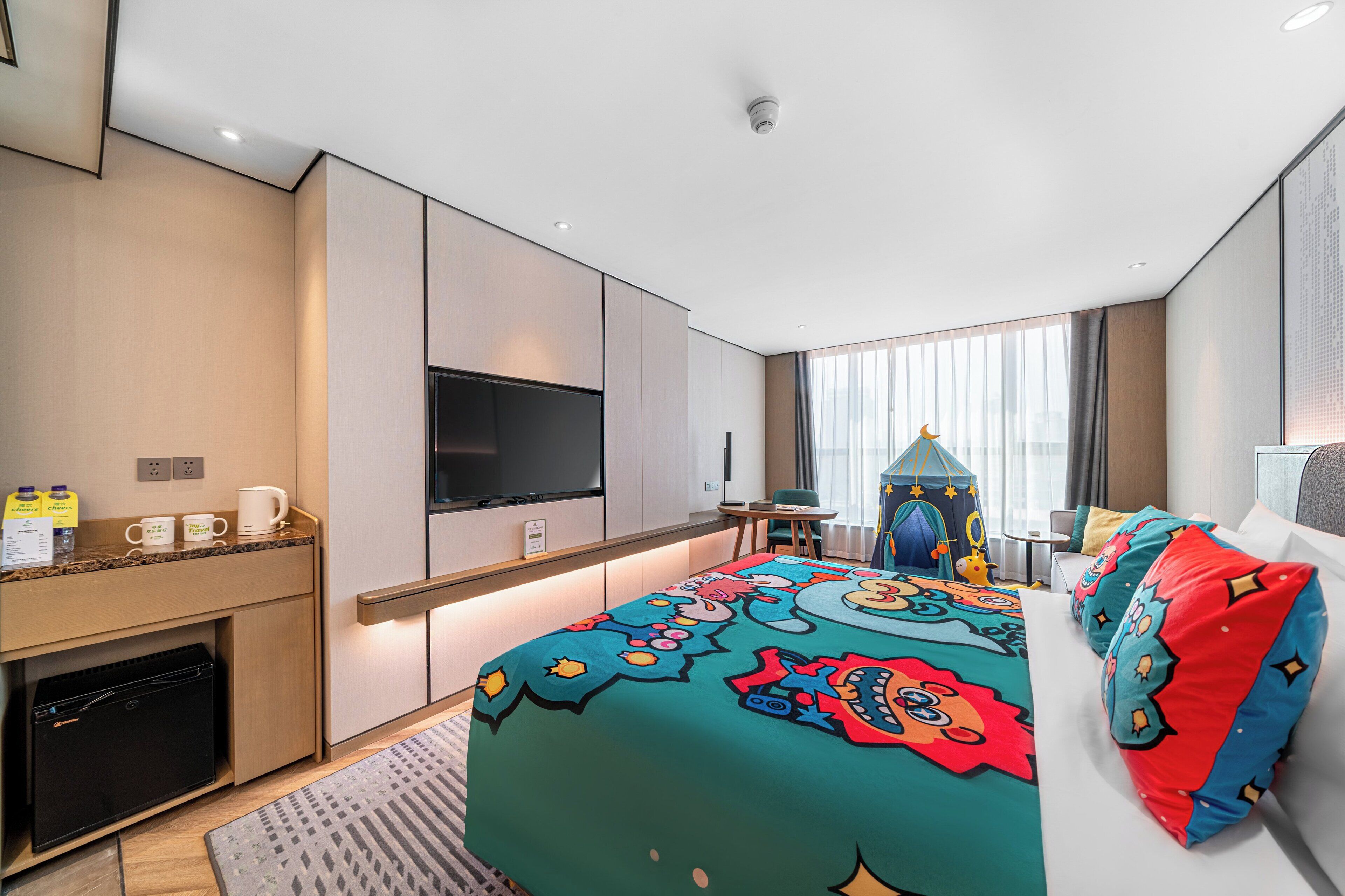 A modern hotel room with a large bed, a flat-screen TV, a desk, and a minibar.
