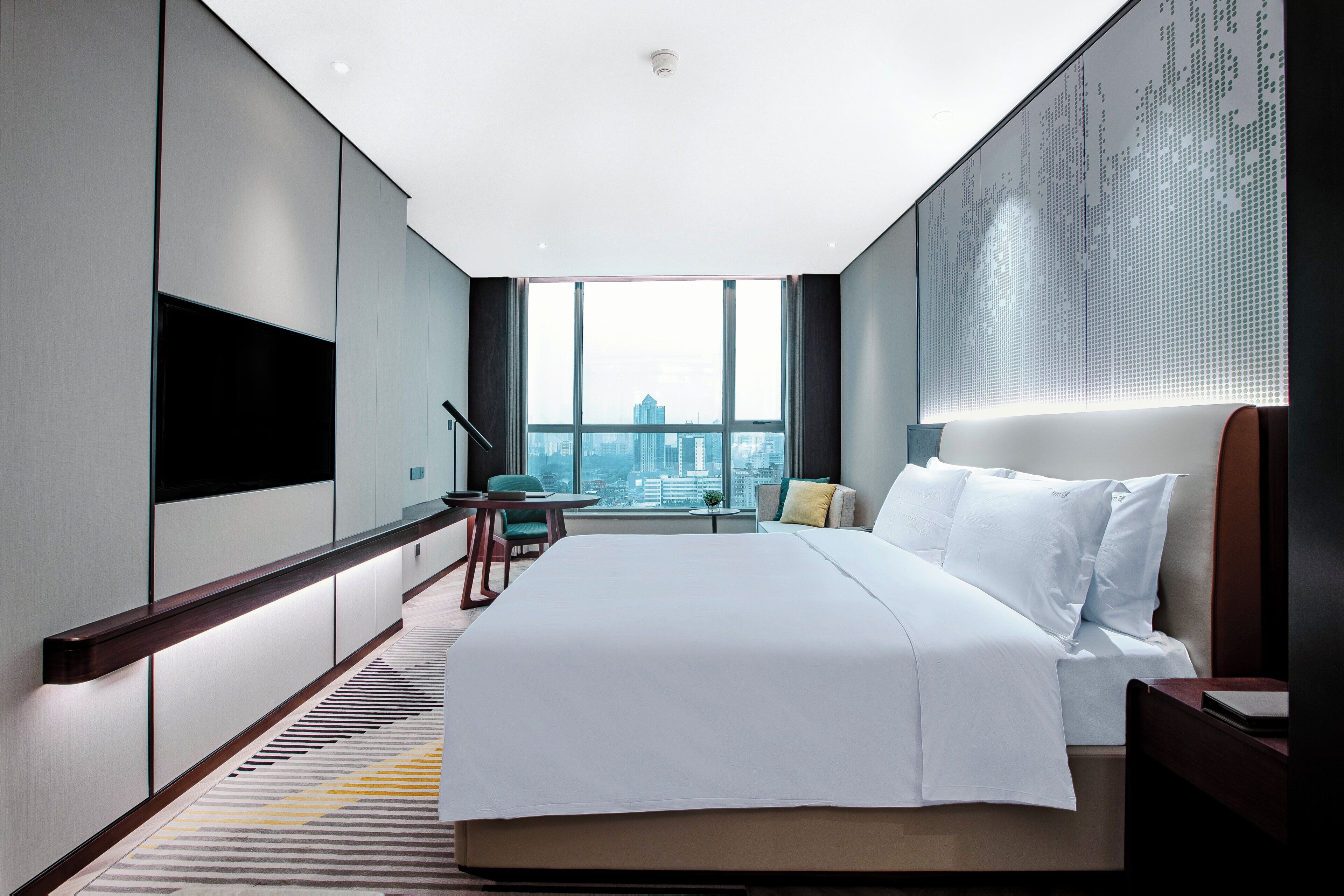 Habitació d'hotel moderna amb un llit gran, una taula de treball i vista a la ciutat.