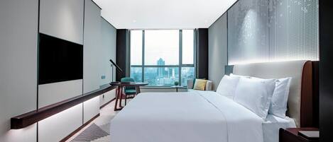 A modern hotel room with a large bed, a desk, and a view of the cityscape.