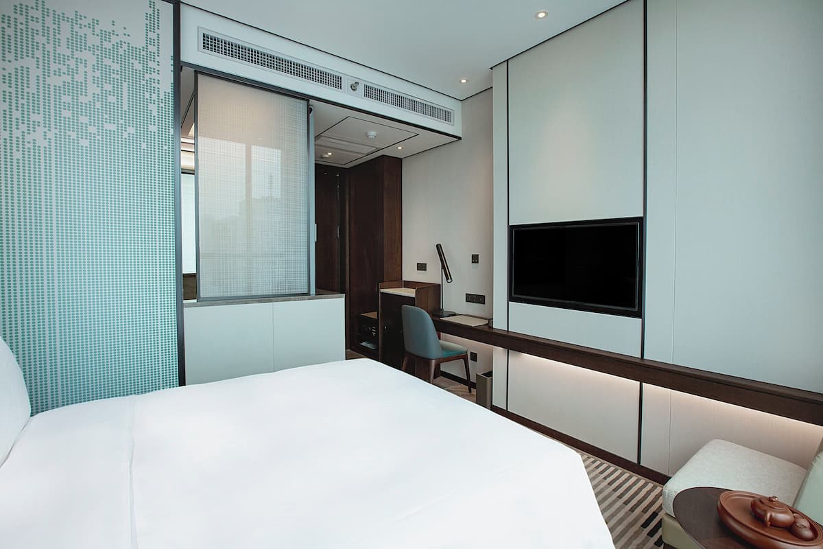 Ein modernes Hotelzimmer mit Bett, Schreibtisch, Stuhl, Fernseher und einer kleinen Sitzecke mit einer Schale.