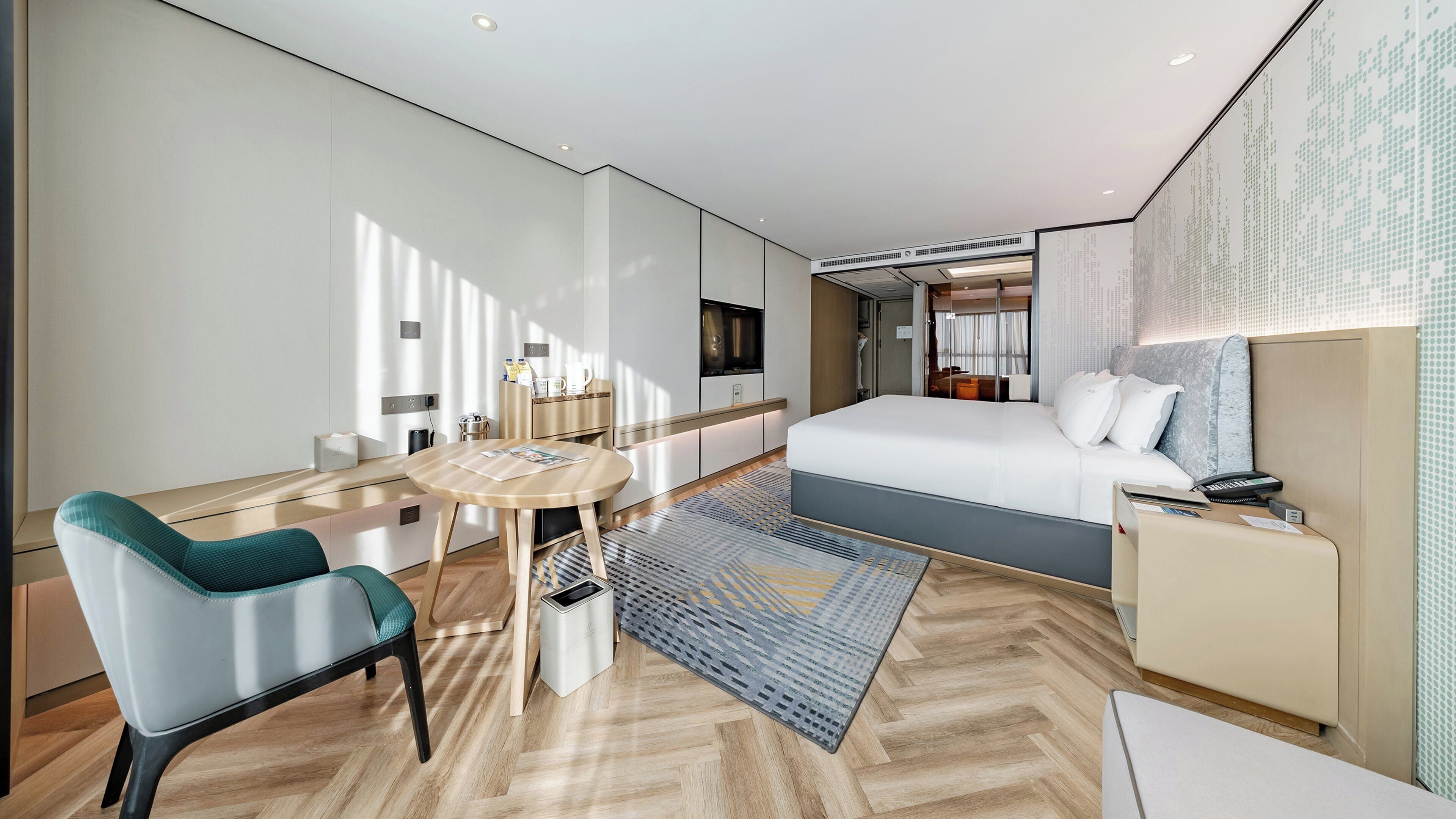 A modern hotel room with a large bed, a desk with a chair, a small table, and a TV.