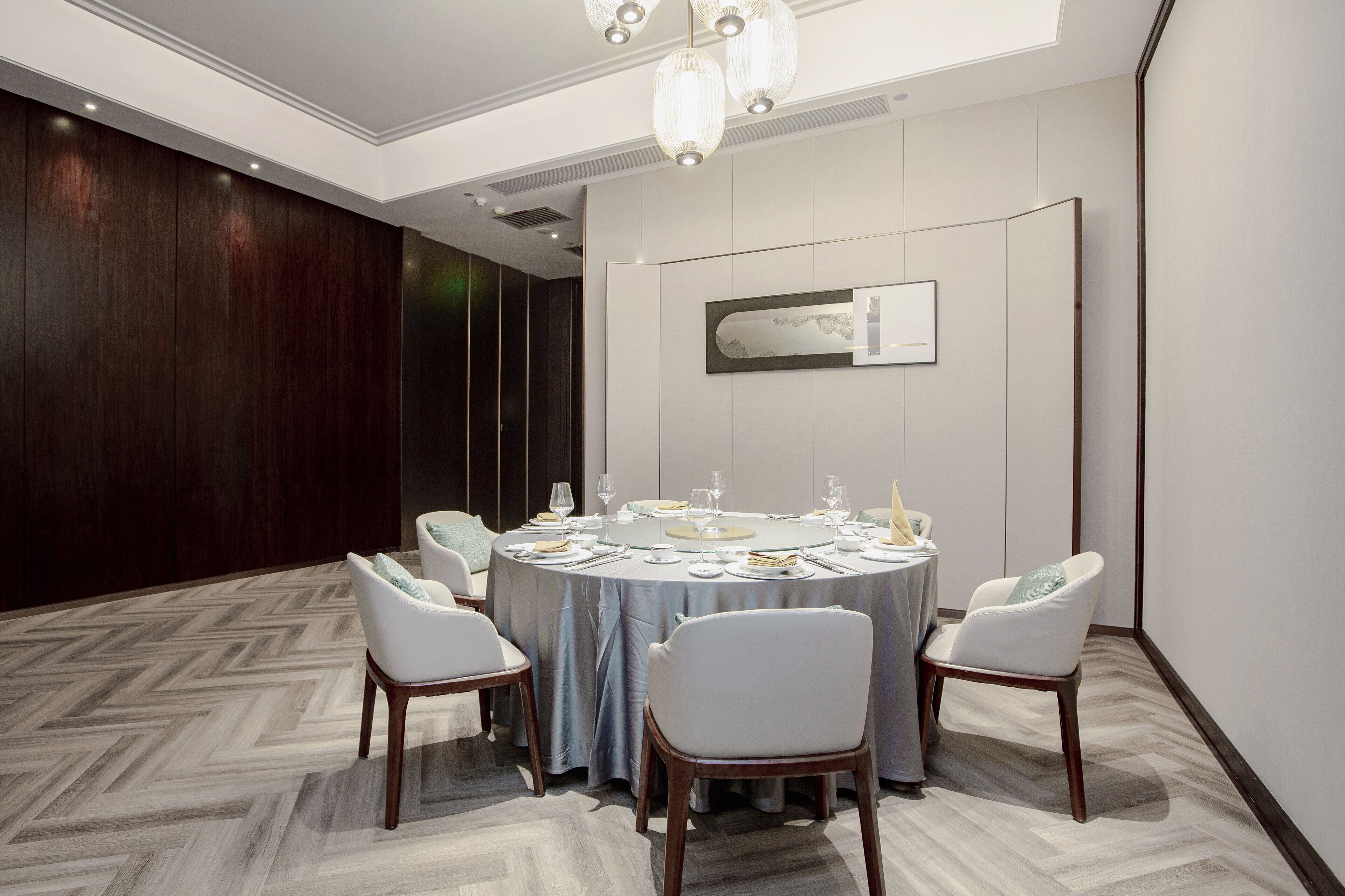 A conference room with a round table set for a meeting, surrounded by white chairs, and a modern chandelier.
