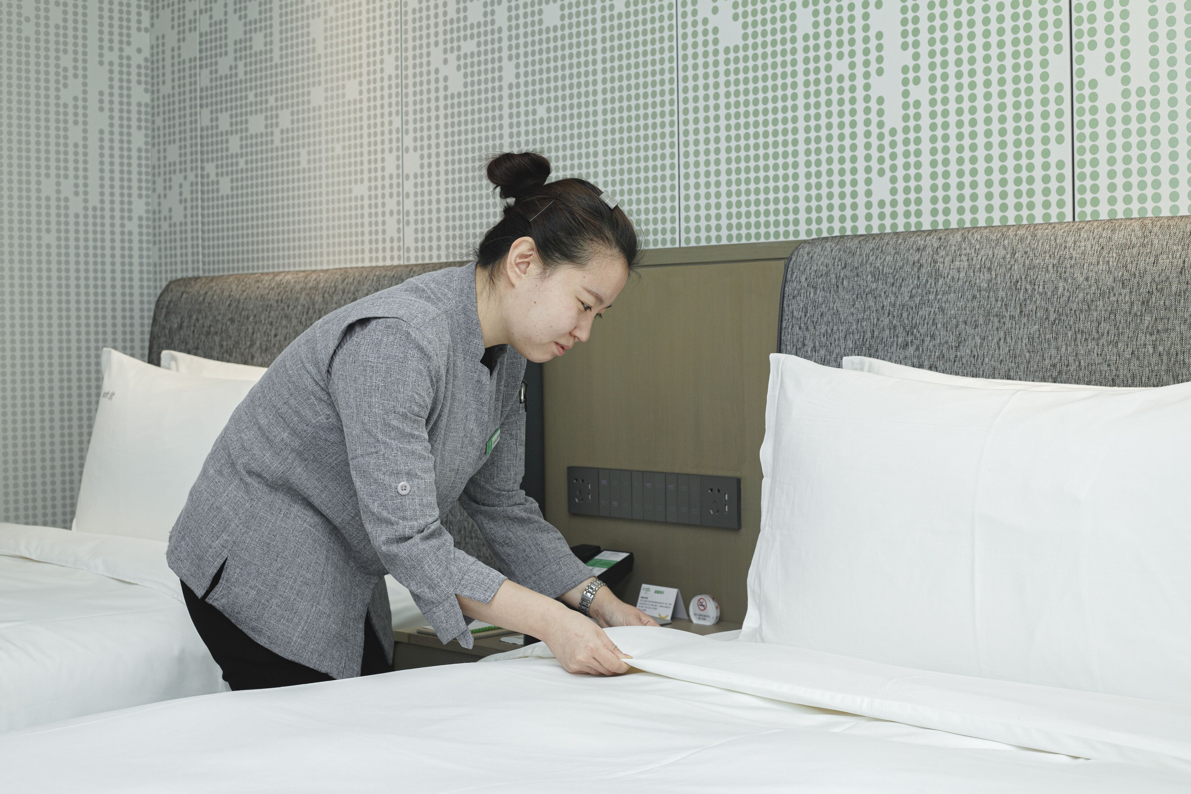 A person adjusting a bed in a hotel room with a patterned wall and a control panel on the headboard.