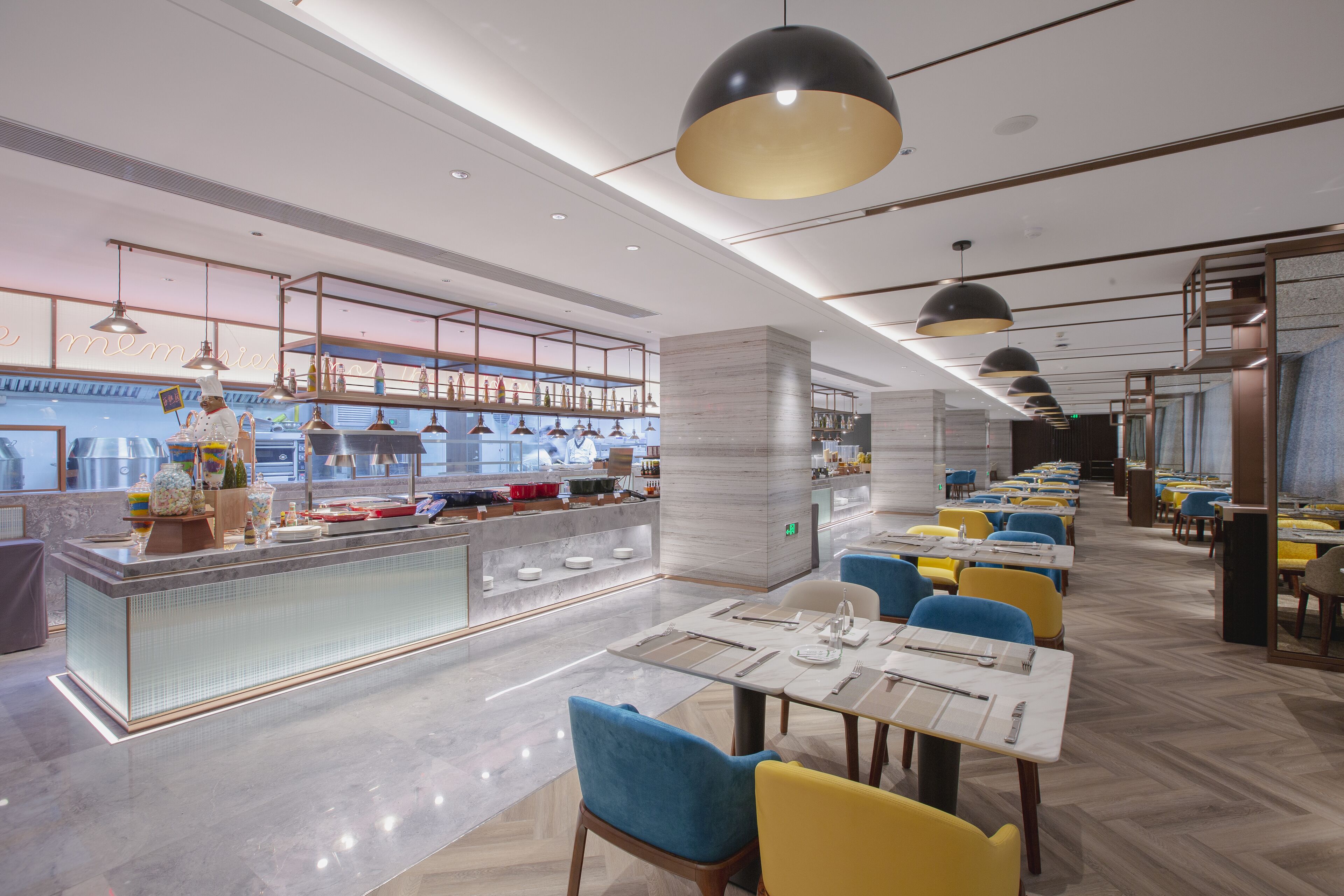 A modern restaurant with a long counter, blue and yellow chairs, and pendant lighting.