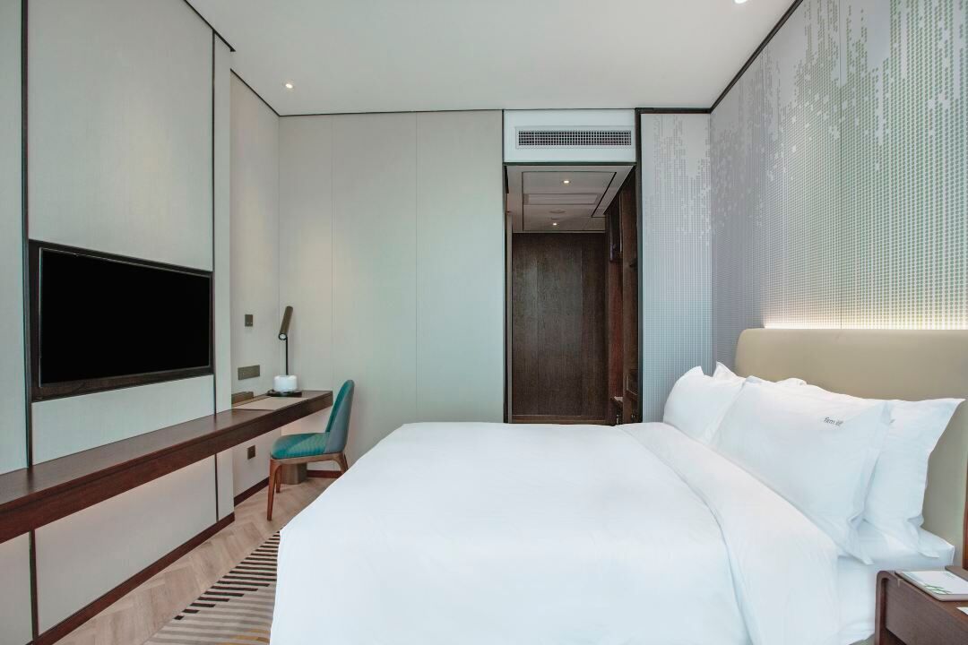 Una habitación de hotel moderna con una cama grande, un televisor de pantalla plana montado en la pared, un escritorio con una silla y un vestidor.