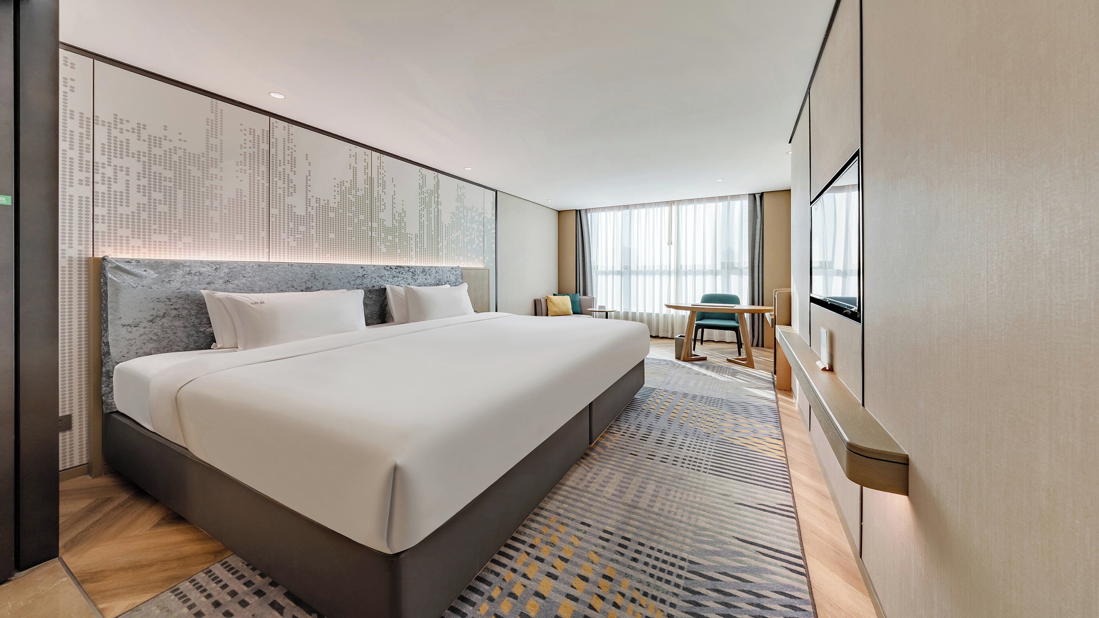 A modern hotel room with a large bed, a desk, and a TV.