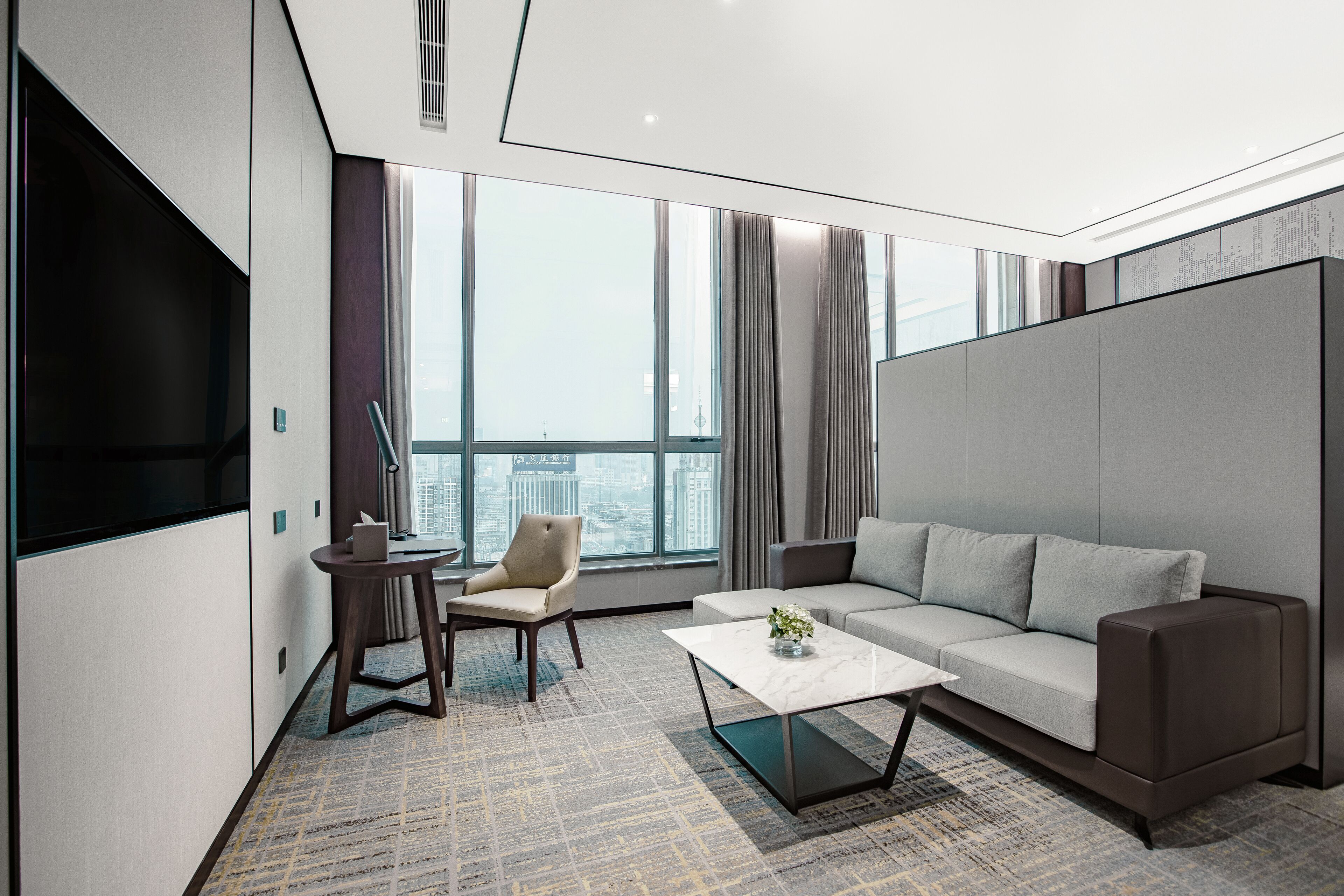 Ein modernes Hotelzimmer mit großem Fenster, einer Couch, einem Couchtisch und einem Fernseher.