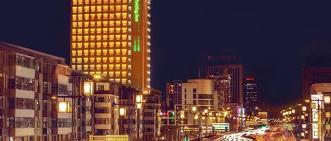 A high-rise hotel with illuminated windows and a prominent green sign.