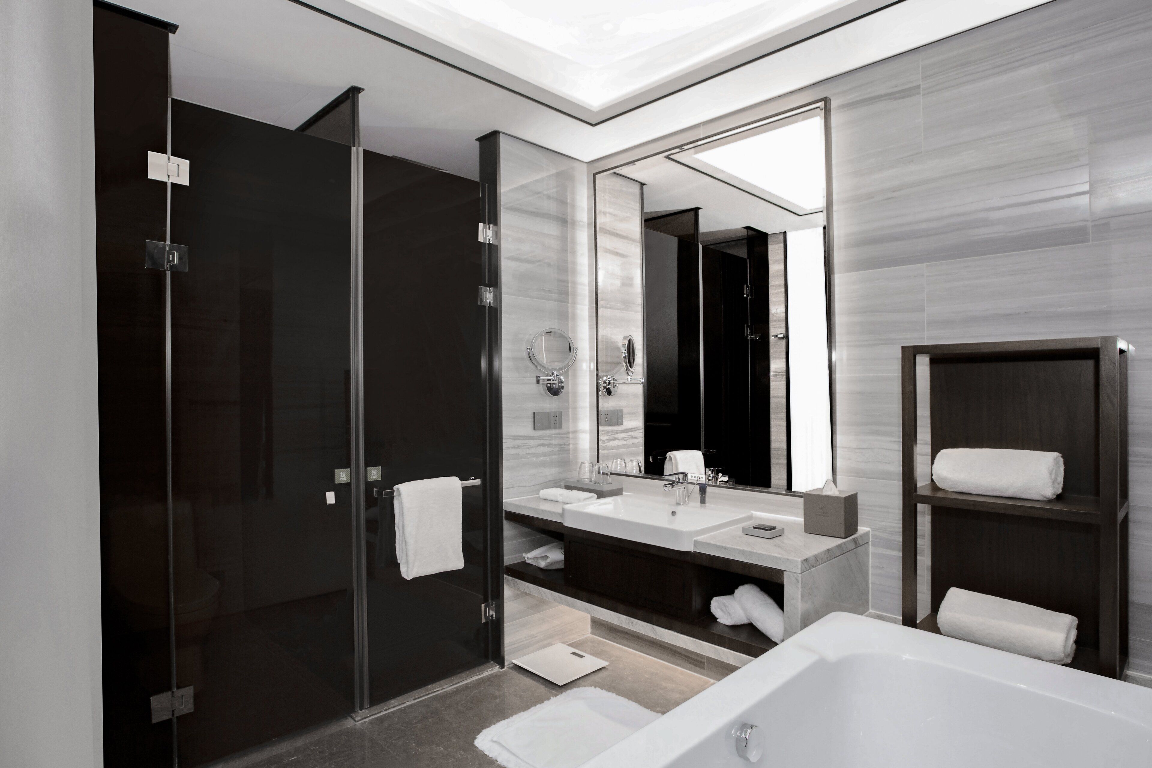 A modern bathroom with a glass shower enclosure, a large mirror, a white bathtub, and a dark wood vanity.