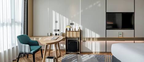 A modern hotel room with a bed, a desk, a chair, a coffee station, and a TV.