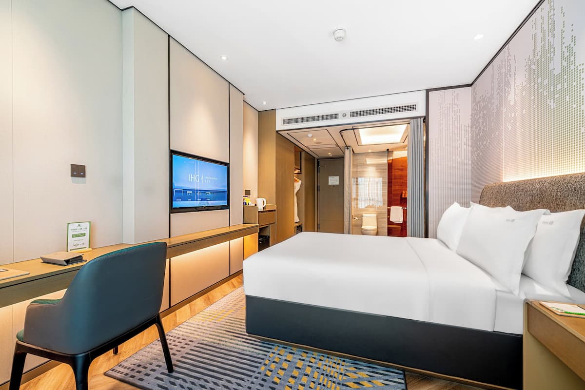 Ein modernes Hotelzimmer mit einem großen Bett, einem Schreibtisch, einem Stuhl und einem Fernseher.