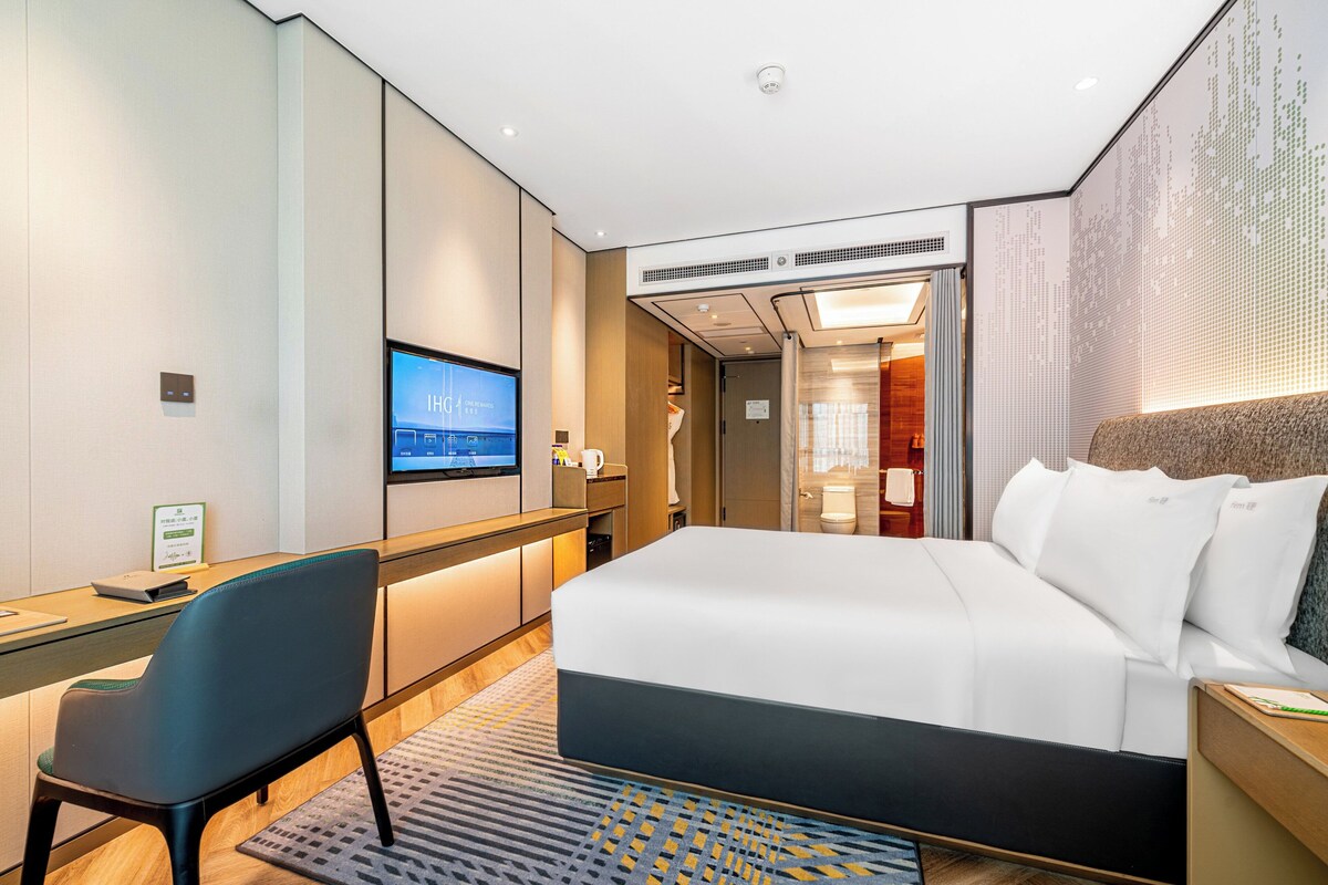 A modern hotel room with a large bed, a desk, a chair, and a television.