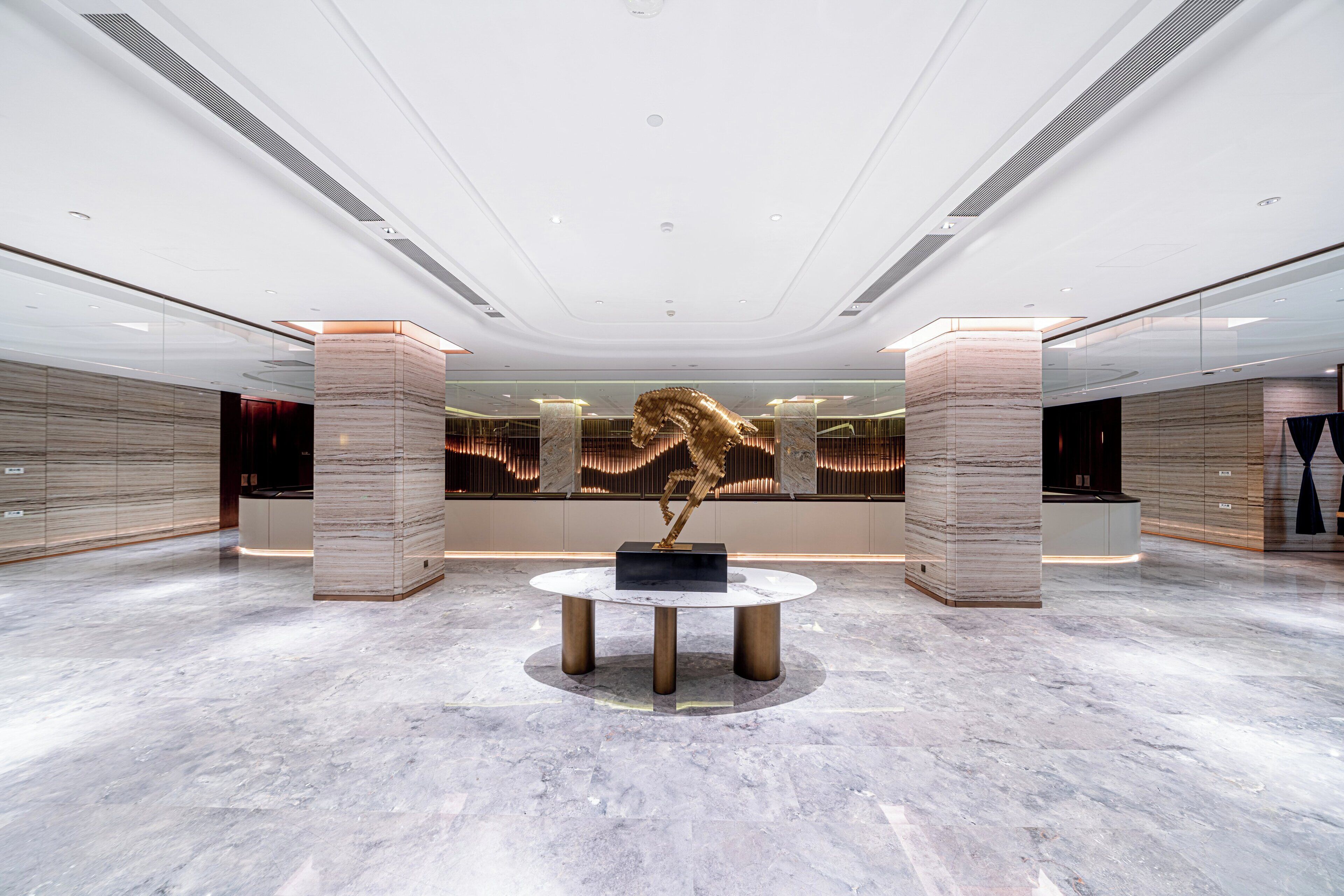A spacious lobby with a marble floor, a central round table, and a large abstract sculpture.