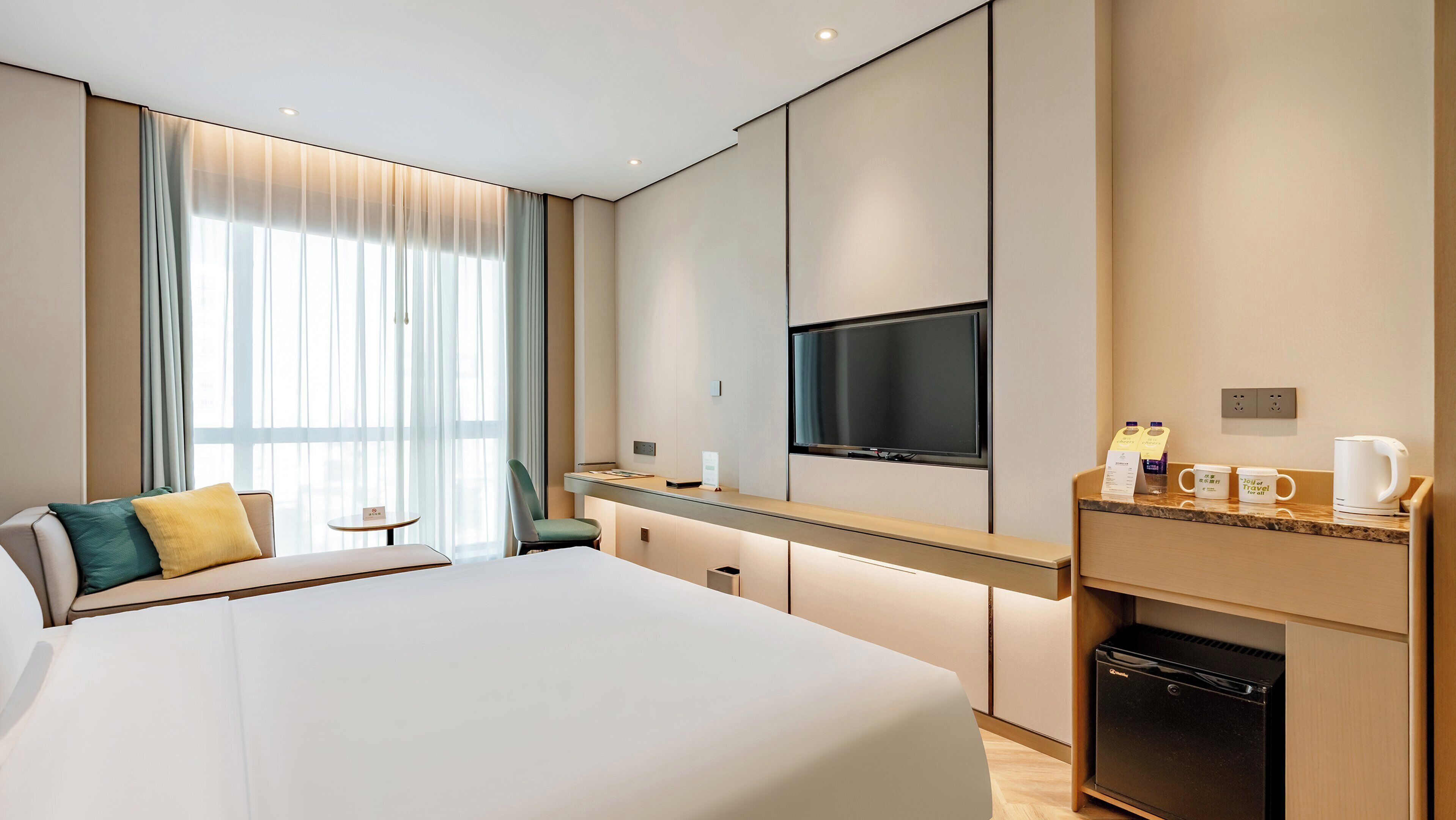 A hotel room with a large bed, a desk with a flat-screen TV, a coffee maker, and a mini-fridge.