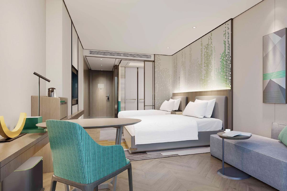 Ein modernes Hotelzimmer mit Bett, Schreibtisch, Sessel, Sofa und einem Wandbild.