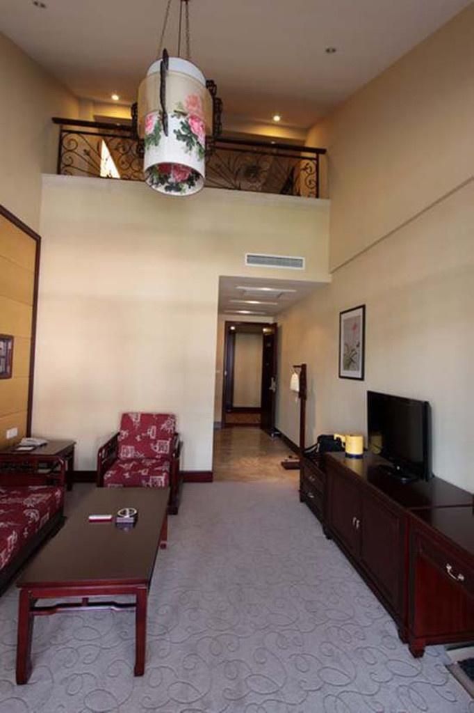 A hotel room with a sofa, a coffee table, a TV, a cabinet, and a decorative hanging lamp.