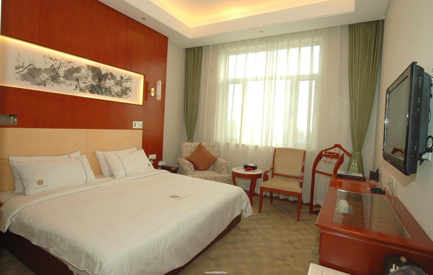 Habitación de hotel con una cama grande, un escritorio, una silla, un televisor y un cuadro en la pared.