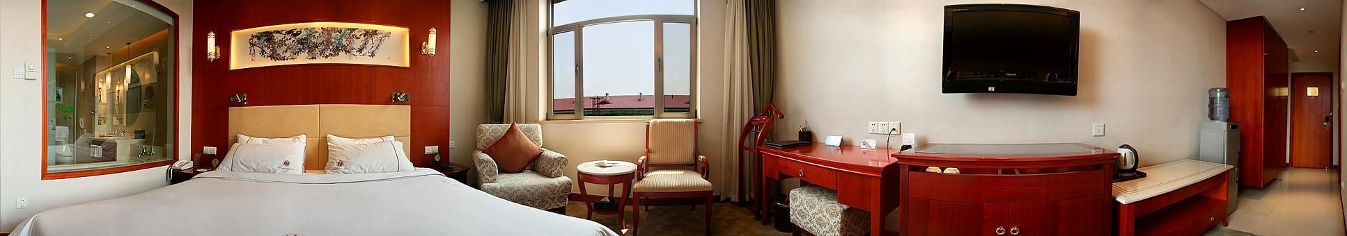 Ein Hotelzimmer mit einem großen Bett, einem Schreibtisch mit Stuhl, einem Fernseher und Blick nach außen.