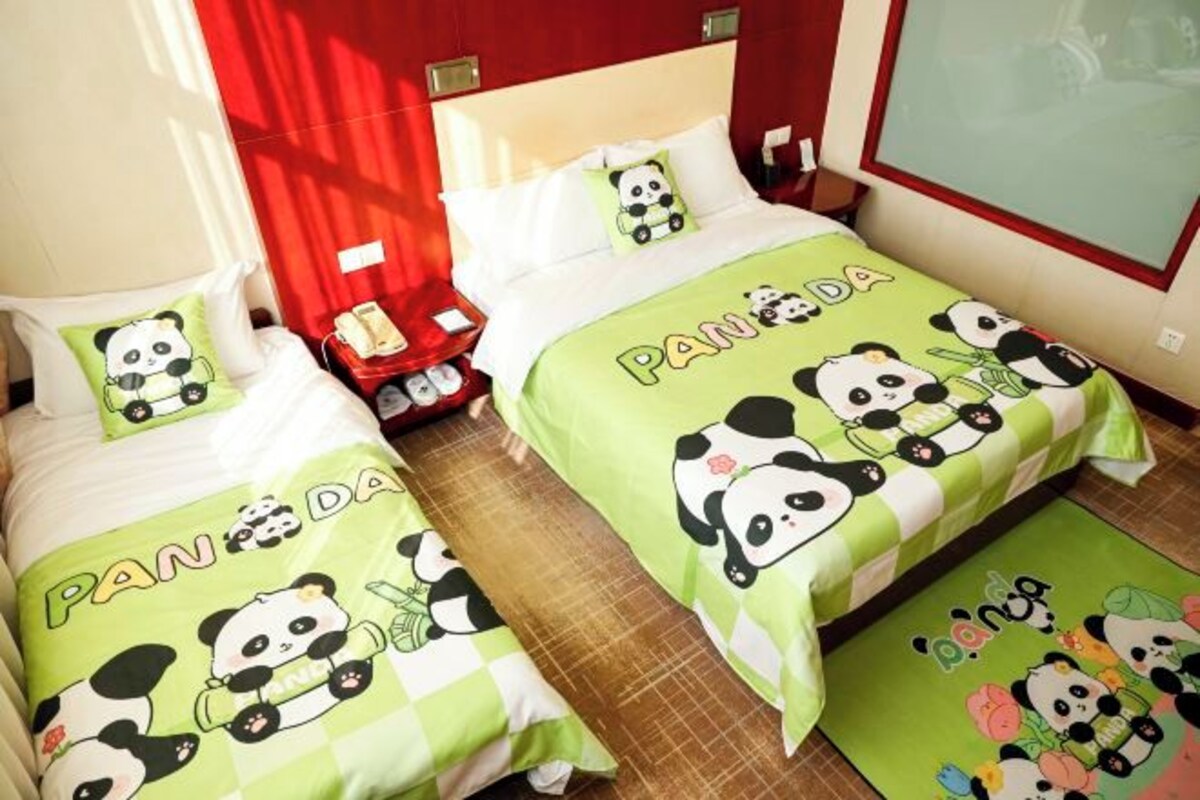 Deux lits jumeaux avec une literie verte ornée d’illustrations de pandas et du mot « Panda » sur les têtes de lit.