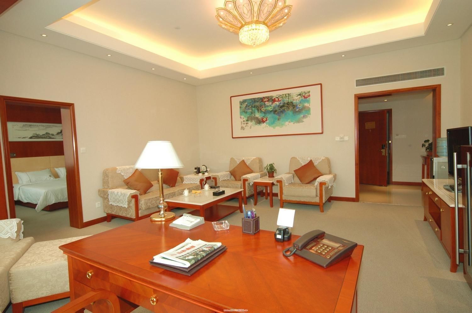 A spacious living room with a wooden coffee table, two sofas, a television, and a painting on the wall.