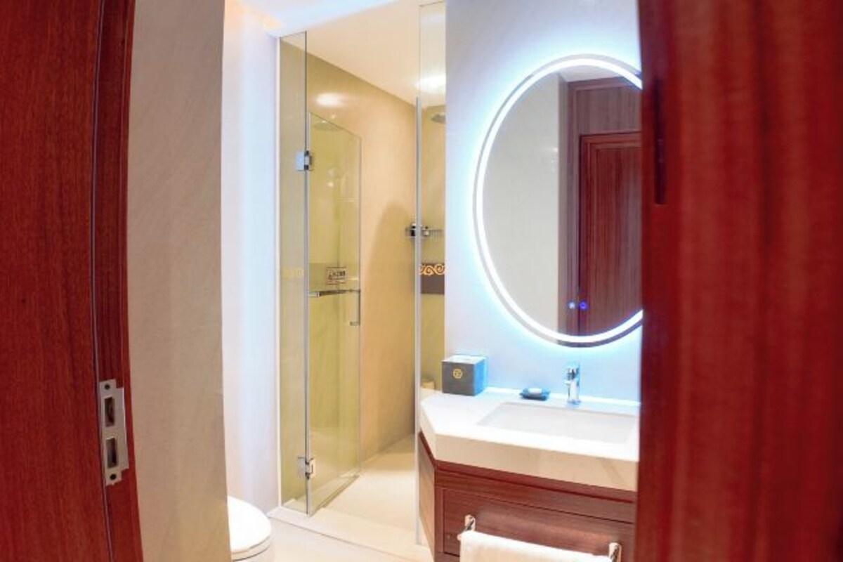 Une salle de bain moderne avec une douche à parois de verre, un grand miroir rond doté d’un éclairage intégré et un meuble-lavabo en bois.