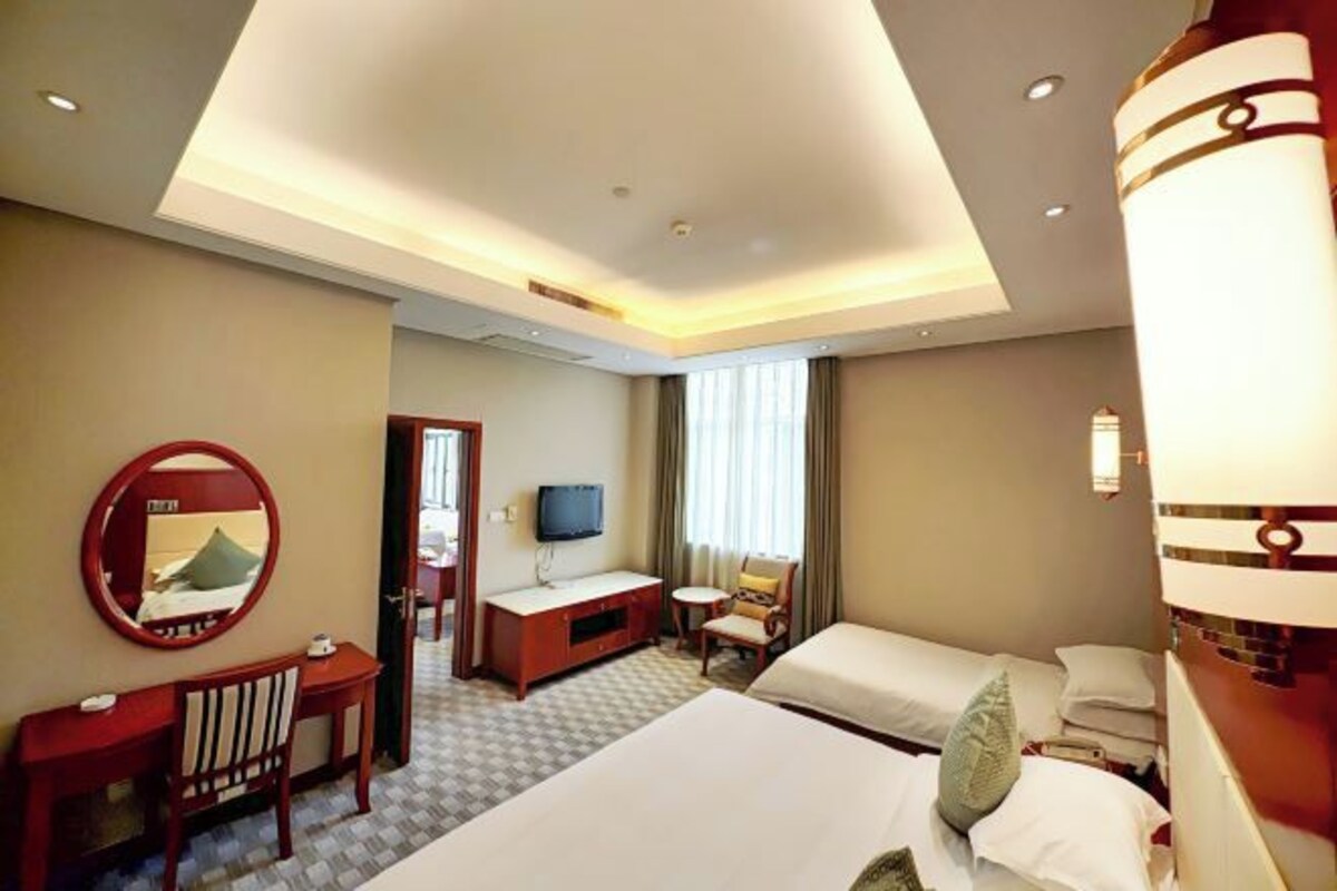 Une chambre d’hôtel avec un lit, un bureau, une chaise, une télévision et une fenêtre avec des rideaux.