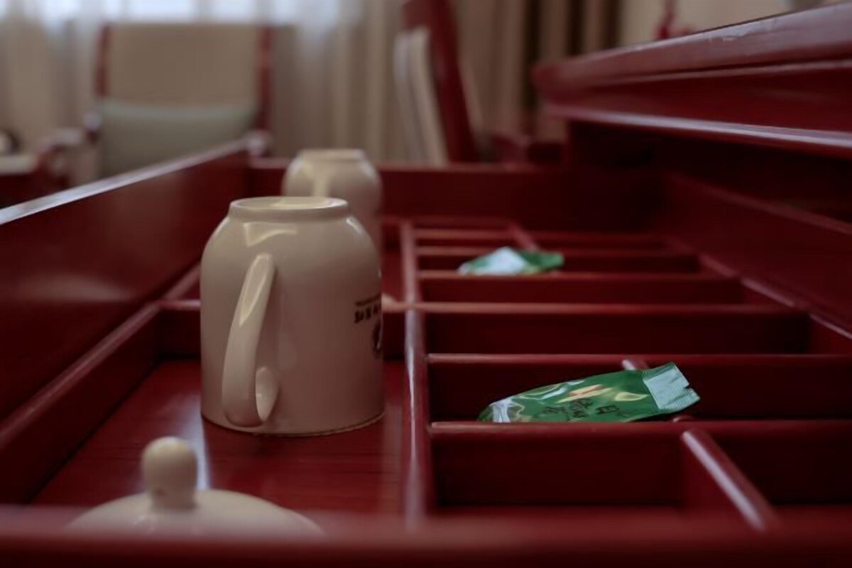 A row of red upholstered seating with a white mug and a green packet on the tray table.