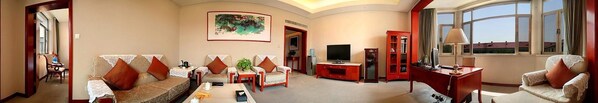 Ein geräumiges Wohnzimmer mit einer Couch, Sesseln, einem Couchtisch, einem Fernseher und einem Schrank.