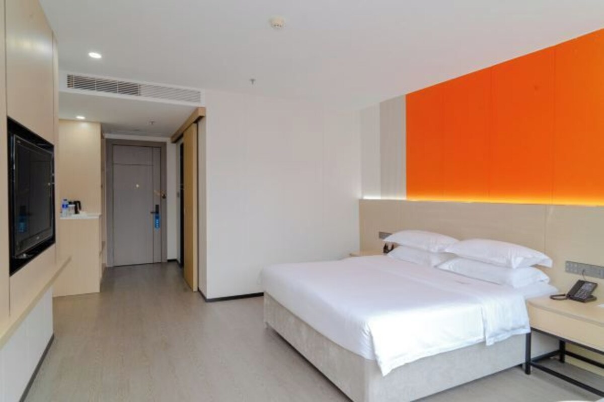 A hotel room with a bed, bedside table, TV, and a door leading to another room.