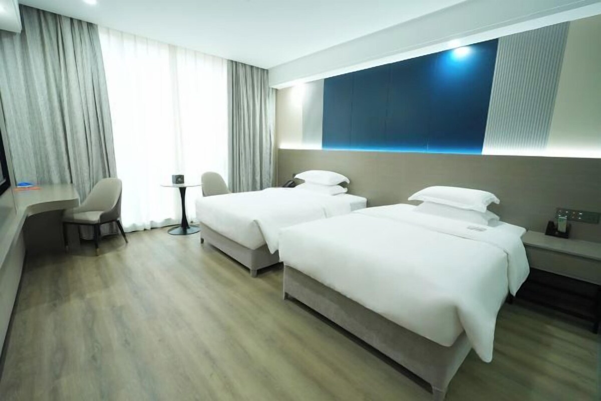 A hotel room with two beds, a desk, a chair, and a large window with curtains.