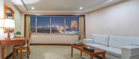 Una sala de estar moderna con un ventanal que ofrece vistas a la ciudad, un sofá, una mesa de centro y un escritorio con una lámpara.