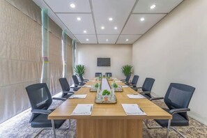 Een vergaderruimte met een lange tafel, stoelen, een projectiescherm en decoratieve planten.