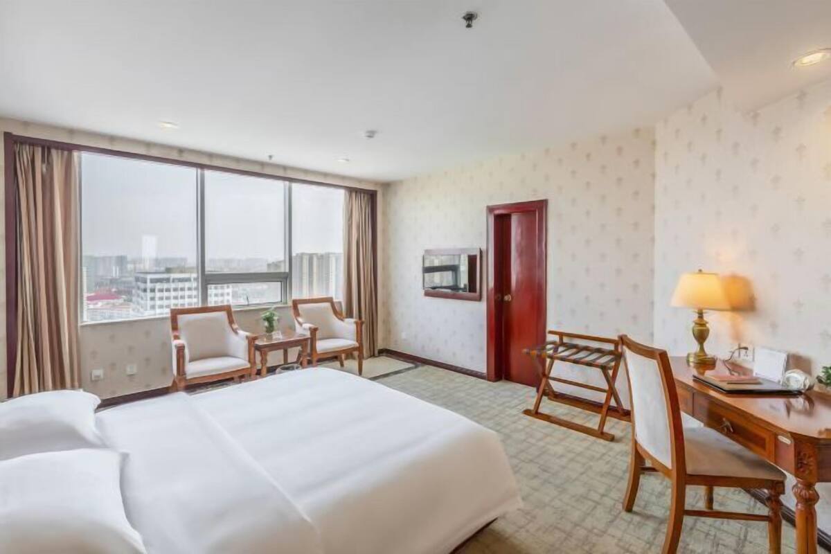 Una habitación de hotel con una cama grande, dos sillas, un escritorio, una lámpara y vistas a la ciudad.