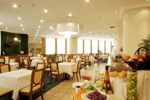 A spacious dining area with multiple tables and chairs, a buffet with various food items, and a large window providing natural light. - Zhongyin Hotel (Baoding)