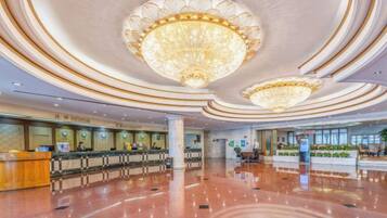 A hotel lobby with a grand chandelier, a reception desk, and a polished floor.