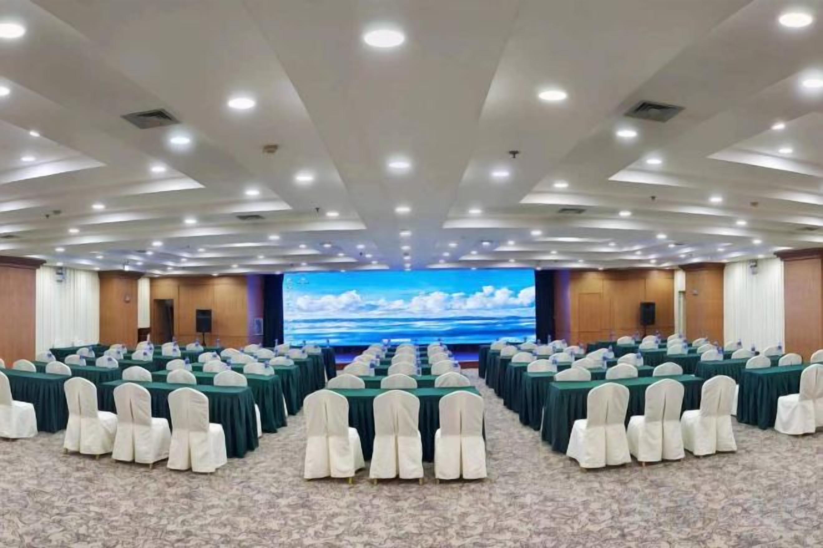 A conference room with rows of tables and chairs, a large screen, and a carpeted floor.