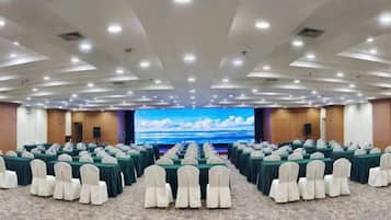 A conference room with rows of tables and chairs, a large screen, and a carpeted floor.