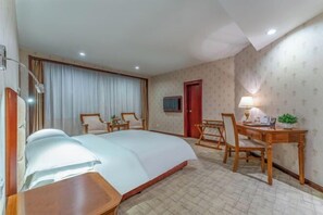 Een hotelkamer met een groot bed, een bureau met een stoel, een kleine tafel met een lamp en een televisie aan de muur.